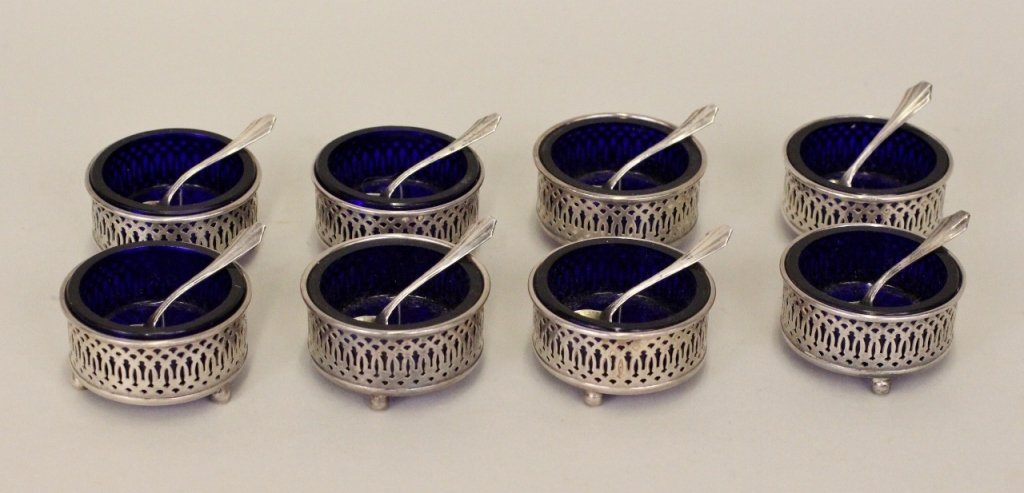 Set of 8 Sterling & Cobalt Salts: Salt cellars with reticulated sterling silver holders raised on three ball feet, cobalt glass inserts within. Each holder marked "STERLING" on bottom. With eight small salt spoons of shell form marked