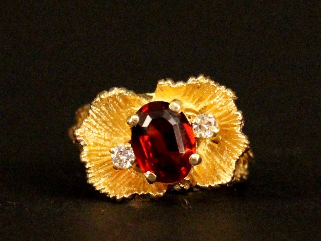 14k Gold, Garnet & Diamond Ring: Ladies 14k yellow gold ring with flower form decoration with an 8x6 oval garnet gemstone at center with two 2.4mm accent diamonds, one is GSi2 and the other is Hi1 totalling .12 ct. Marked on interior