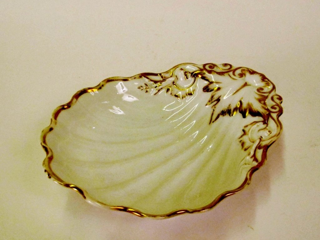Old Paris Style Porcelain Serving Dish: White porcelain serving dish or bowl of shell form with gilt rim and accent decoration in the form of a leaf on one end flanked by scrolled foliate design. Unmarked. Height 2.5 inches, width 10.4 inch