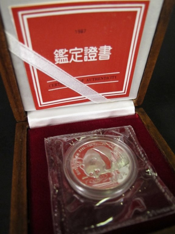 1987 China 1 Oz. Platinum 100 Yuan Coin: China, 1987. 100 yuan coin composed of 1 ounce of platinum. Coin with imagery on one side of a panda bear drinking water by a bank marked with bamboo trees. Back of coin with Hall of Prayer for Good H
