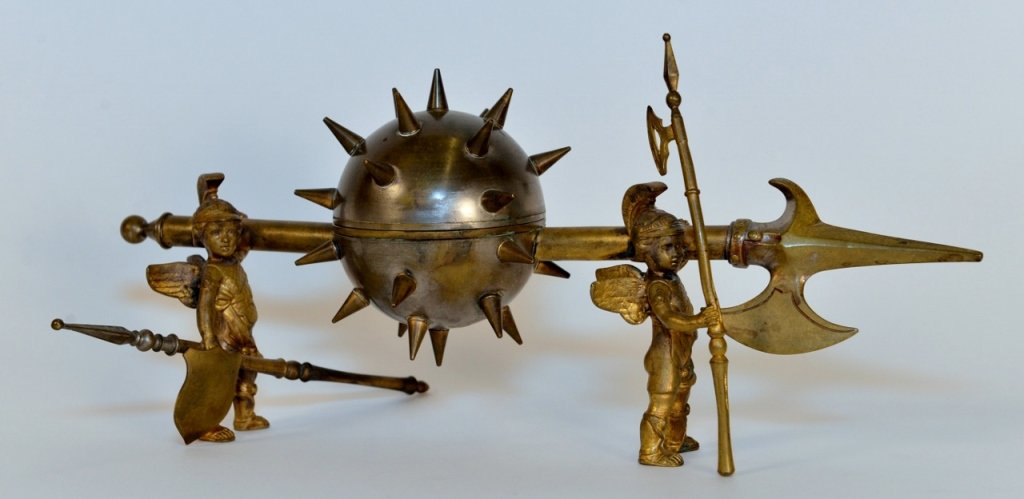 Brass Figural Winged Warrior Inkwell: 20th century. Inkwell within a round spiked ball flail weapon form with hinged top to ink well vessel within. Spiked flail in middle of speared weapon form being held up by two small winged warriors o