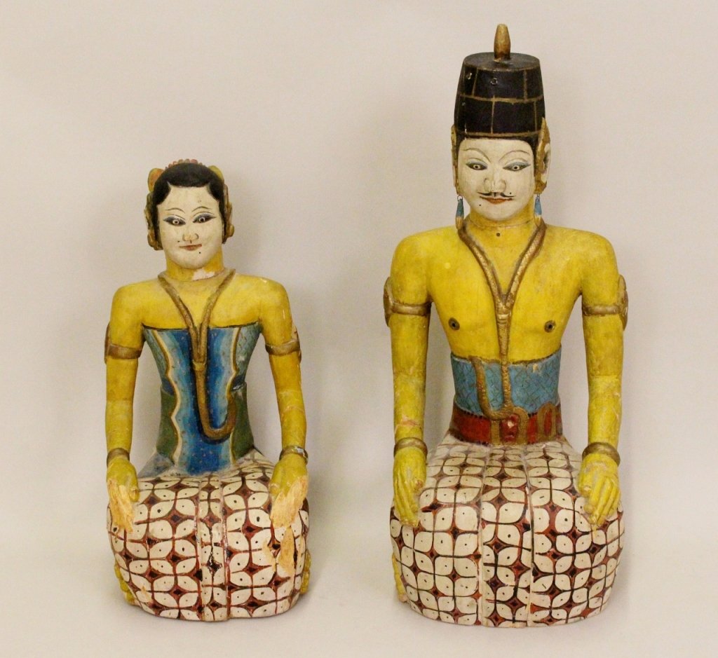 Pair of Polynesian Wooden Figures: Polynesian wooden polychromed seated figures of a man and a woman depicted wearing matching sarongs over stylized yellow bodies. Each figure adorned with gilt tone necklace, earrings, bracelet and arm
