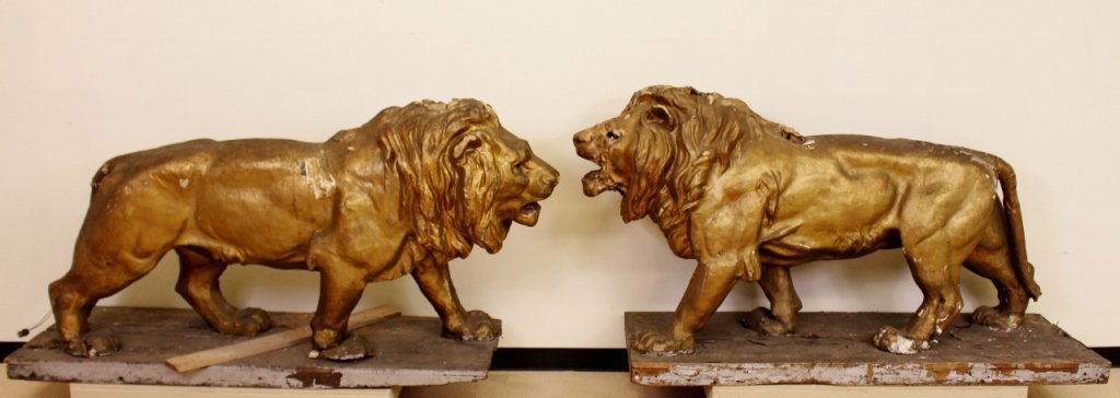 Monumental Pair of Papier Mache Lions: Two large sculptural companion lions composed of papier mache and with a painted metallic gold finish with antiqued and weathered patina. The lions each measure 39 inches high, 69.5 inches in length, 