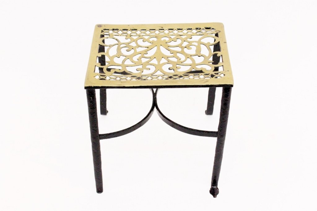 Brass and Iron Fire Trivet: Fire trivet with rectangular brass metal top with scrolled foliate and arched detail above a black painted cast iron frame with curved cross supports. Leaf foliate form feet (one damaged and missing).