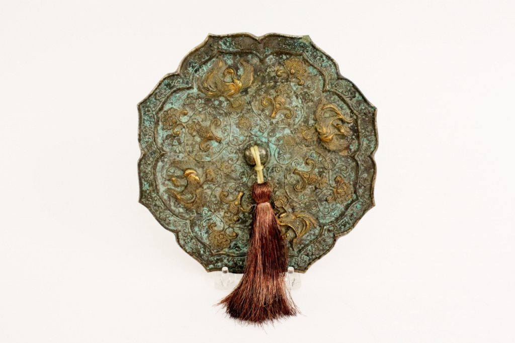 Chinese Bronze Mirror w/Bird & Floral Motif: Chinese bronze mirror of quatrefoil form with hanging tassel at center. Verso of silvered mirrored surface with four feathered birds that alternate with floral and scrolled decoration, remnants of gil