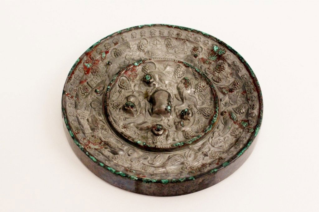 Chinese Bronze Mirror w/Animal & Grape Motif: Chinese bronze circular mirror with cast in Tang Dynasty style with a canted edge and concave band of scrolling lotus flowers over an outer band of grapes and birds. Center section containing lions an