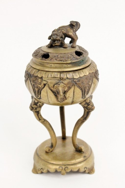 Oriental Metal Incense Burner: Oriental footed incense burner composed of bronzed metal. Circular pierced lid with foo dog finial above bowl container raised on three legs with scrolled feet on circular base with scalloped edges on