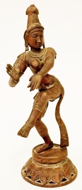 Bronze Thai Figurine of a Female Temple Dancer: Depicted standing on one foot while balancing in a decorated costume with necklace, earrings, headpiece, armbands and anklets; raised on a circular base. Height including base 9 inches.
