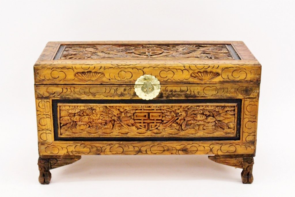 Chinese Carved Camphor Wood Chest: Chinese carved camphor wood chest with hinged lid decorated with two dragons flanking a seal. Scene accented with stylized clouds and demarcated by black painted border within border with cloud motif.