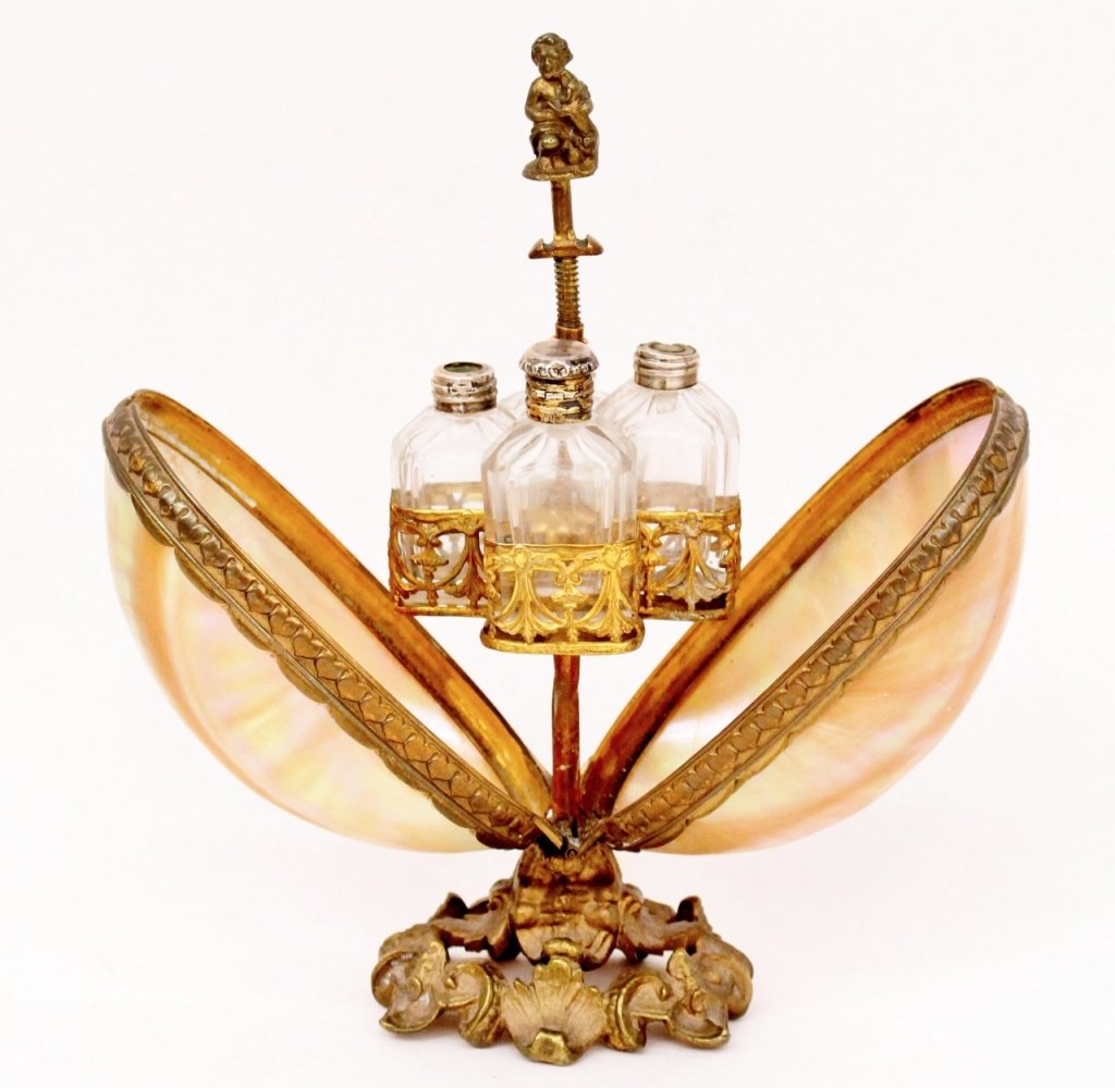 Mother of Pearl Oyster Form Perfume Holder: Mother of pearl oyster form perfume holder with shell sides that open to reveal metal curtained swag decorated metal holders for four small glass vials for storing perfume below nude putto with dog at