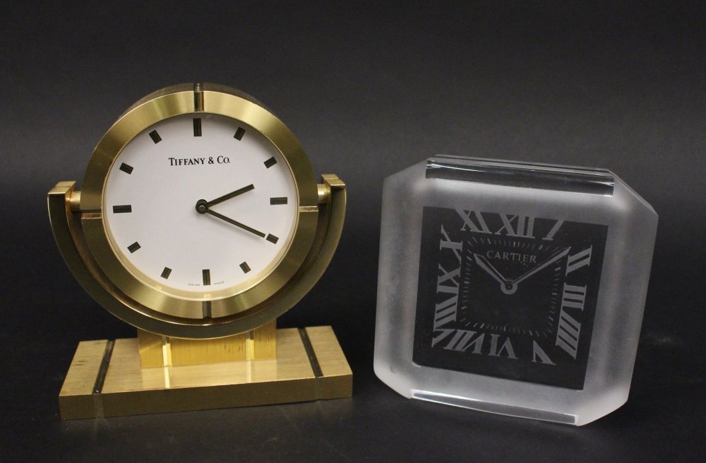 2 Designer Clock Items, Tiffany & Co. and Cartier: 20th century. Group of two clock related items comprising of a Tiffany & Co Swiss made desk clock with brushed gold tone finish throughout with adjustable white clock face; and a glass desk or office 