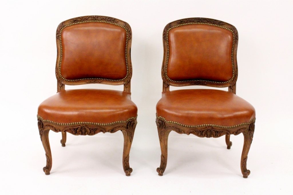 Pair of Louis XV Style Leather Slipper Chairs: France. 20th century. Pair of French Louis XV style slipper chairs with cartouche shaped floral carved crestrail, the back and serpentine seat covered in leather with large brass nailhead trim, the co