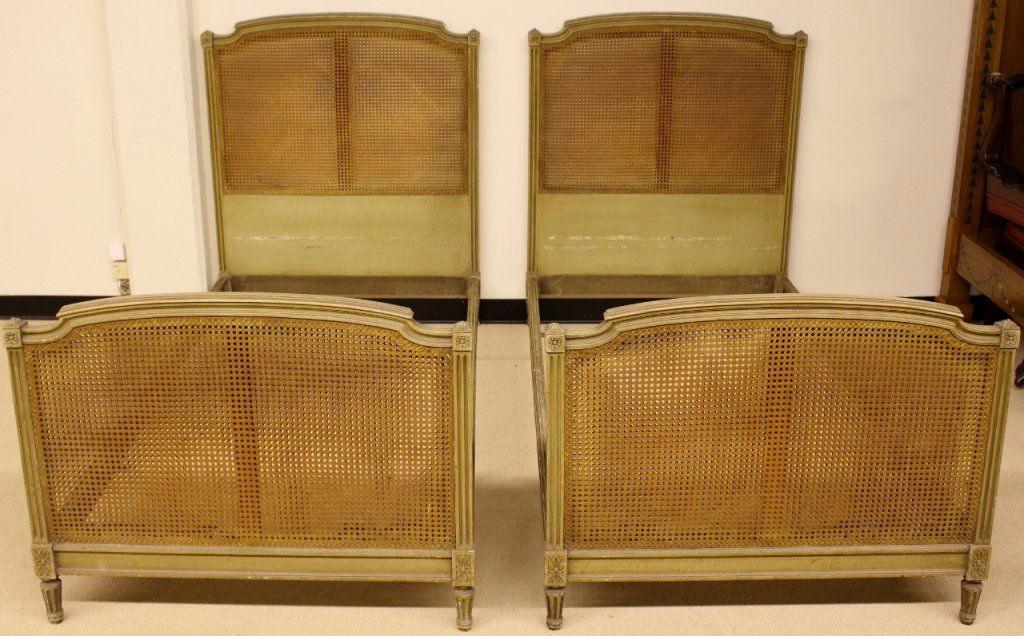Pair of French Painted & Caned Twin Beds: French, 20th century. Pair of twin sized beds with caned headboard and footboard with fluted and patera block details. Approximate height 47.25", width39.75", depth 78.75". Please consult the addition
