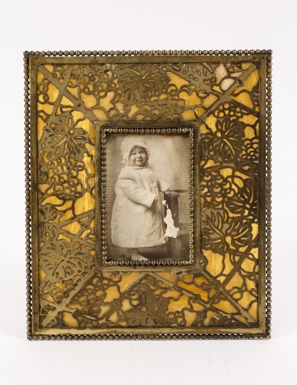 Tiffany Studios Grapevine Picture Frame: American (New York), Early 20th century. Tiffany Studios gilt bronze and favrile glass table top picture frame with grape vine pattern with reticulated or pierced design surrounded with beaded border.