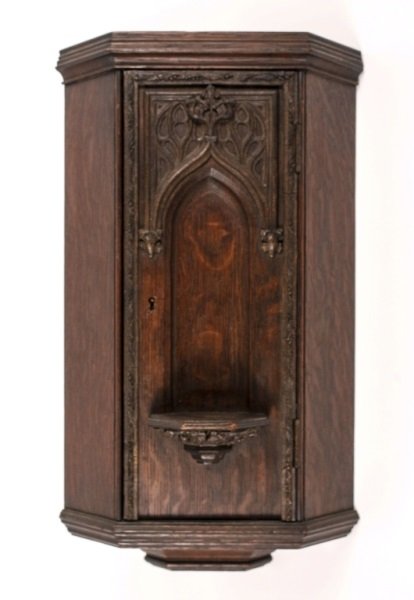 Carved Oak Wall Hanging Small Corner Cabinet: Likely English, 20th century. Stained oak wood small corner cabinet with recessed Gothic style niche on hinged front door. Wall storage and display cabinet with carved undulating border decoration on 