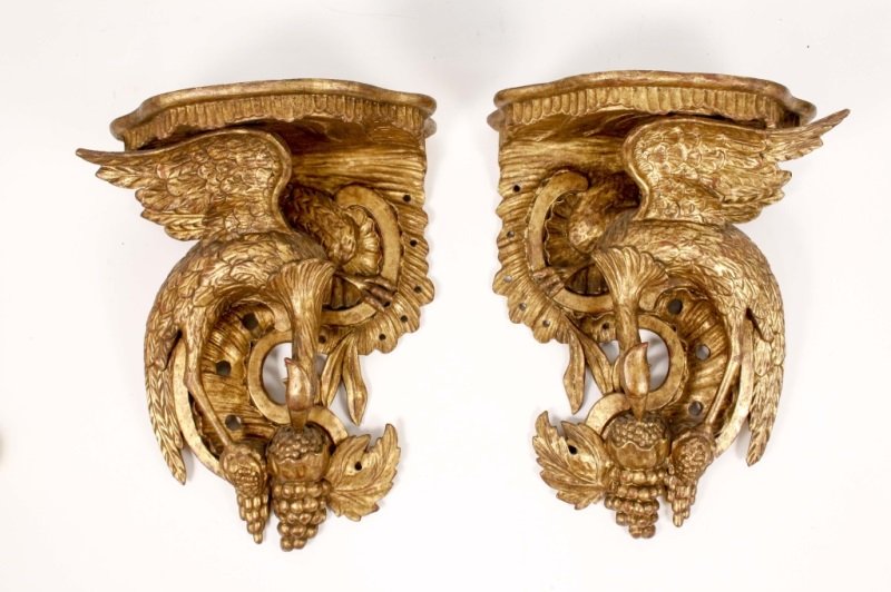Pair of Continental Carved & Gilt Bird Brackets: Continental, 19th century. Pair of matching hand carved and gilt figural wall brackets with shaped top with ribbed undulating apron supported by feathered wings of bird, likely phoenix, eating fruit a