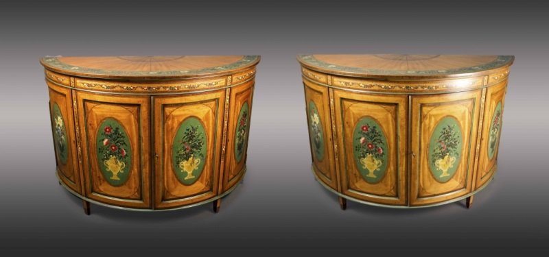 Pair of Painted Satinwood Demilune Cabinets: English, circa 1900. Pair of Edwardian painted satinwood demilune cabinets with fanned and painted floral decoration on green on top above floral and leaved swags above four curved hinged paneled door