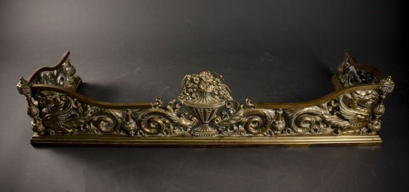 English Brass Fire Fender, 19th C.: English, 19th century. Ornate brass metal fire fender with pierced decoration of floral urn at center of front flanked by scrolled foliates, smaller acanthus leaf tip encrusted bottles and winged gryp