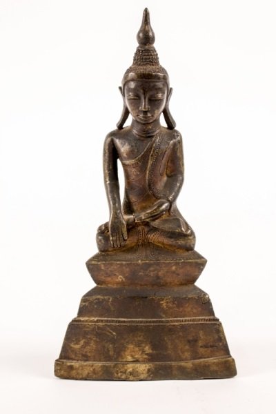 Sino Tibetan Bronze Buddhist Sculpture: Sino Tiebtan bronze metal table top sculpture of a seated buddha wearing headdress and with calm facial expression, elongated stylized earlobes and draped robe. Figure seated at top of triangular plin