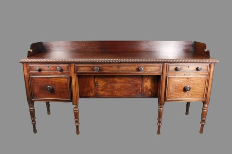 English William IV Mahogany Sideboard: English, Circa 1840. William IV mahogany sideboard with rectangular backsplash with scroll cut ends and exposed dovetails over a long top with gadrooned edge with three frieze paneled drawers, centere