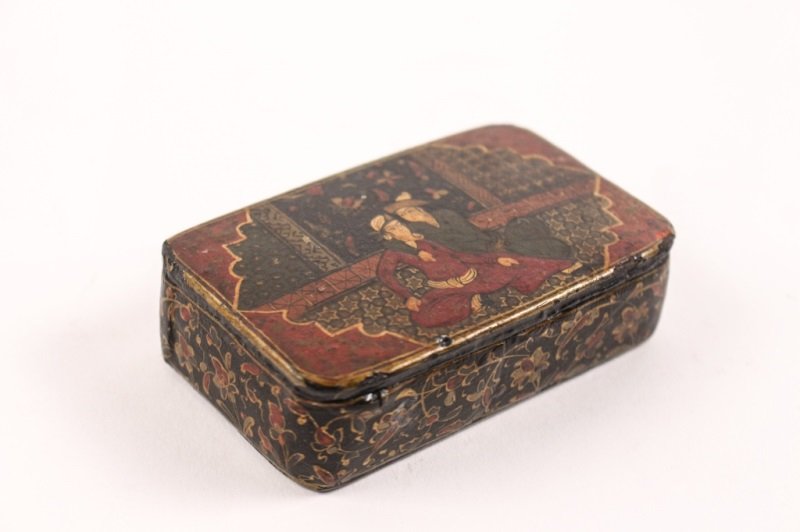 Persian Hand Painted Papier Mache Snuff Box: Persian, Mid to Late 19th century. Hand painted papier mache snuff box of rectangular form with rounded corners. Lid with figural scene with two seated men wearing hats in embrace within interior. Low