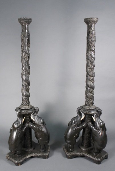 Pair Chinese Ebonized Floor Torcheres w/ Elephants: Chinese. Early 20th century. Pair of painted black wood floor torcheres with hand carved decoration on tripartate base of baby elephants standing on back feet with front feet resting on center column,