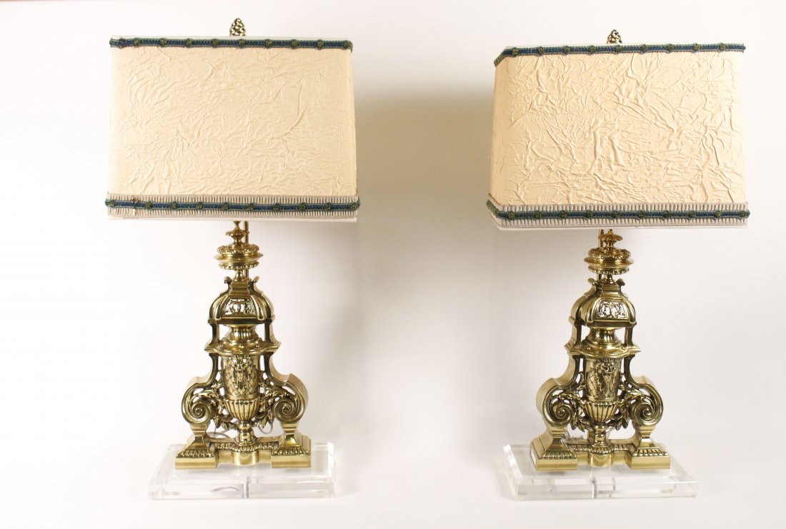 Pair of French Brass Chenet & Lucite Lamps: Pair of French brass chenets or andirons later mounted on rectangular beveled lucite plinth bases and converted into electrified table lamps. Each with a pierced chenet with scrolled accents on sides 