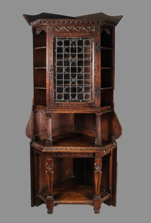 19th Century Gothic Revival Oak Corner Cabinet: English, 19th Century. Gothic Revival stained oak carved corner cupboard or cabinet with shaped pediment over a geometric carved cornice and frieze above a leaded glass door enclosing a shelved interi