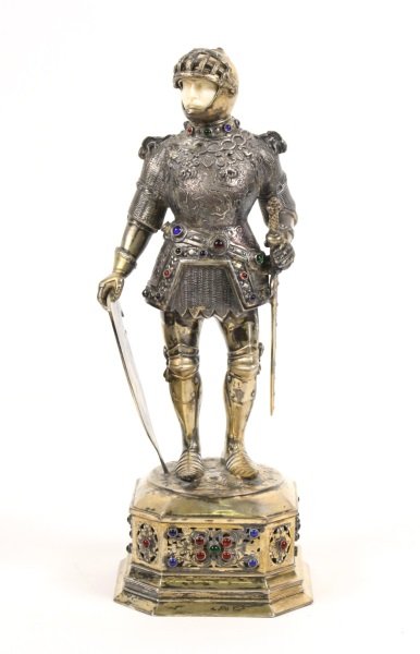 Reproduction Silvered Knight Figurine: 20th century reproduction table top figure of a Germanic Knight with ivory colored face and silvered armor with dragon motif on breastplate and chain mail texturing throughout accented with colored gl