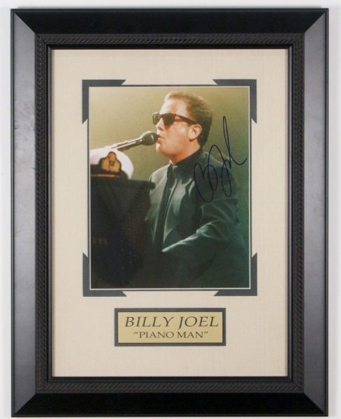 Framed Autographed Photo, Billy Joel: Framed color promotional bust length photograph of musician Billy Joel (American, b. 1949-) playing piano and singing into microphone. Signed in blue ink at right of figure. Framed approximately 19.5"