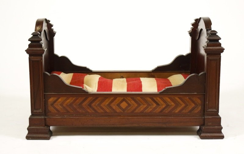Mid-19th C Mahogany Inlaid Doll or Animal Bed: Mid 19th century mahogany doll's bed with arched head and footboard flanked to each side by shaped finials, the side rails inlaid with chevron parquetry. Frame is made to hold a 24-inch doll on the 30