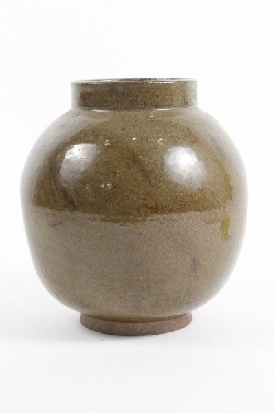 1977 Paul Chaleff Green Glazed Pottery Bowl: Paul Chaleff (American/ New York, 1947- ). An olive green glazed ball form pottery urn with round foot and cylindrical lip, and concave details on two sides of body decorated with unglazed foliate for