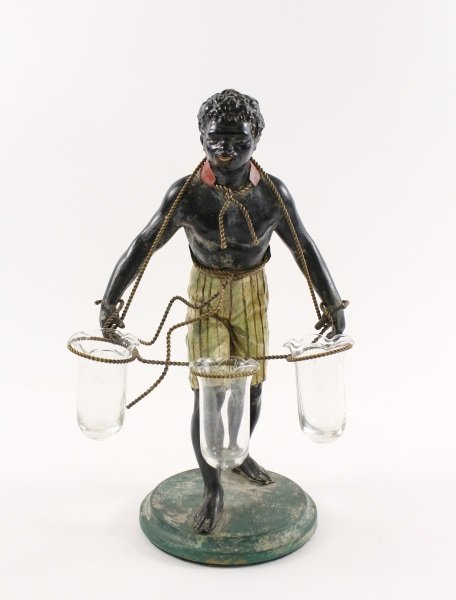 Polychromed Blackamoor Figural Triple Bud Vase: American, first half 20th century. A cast metal figural polychromed blackamoor sculpture depicting a single male wearing green striped short pants, a vest that ties with gold tone rope to neck and wai