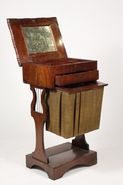 Regency Mahogany Sewing Table: English, circa 1810. Regency mahogany sewing table with shaped, hinged top inset to the interior with mirror and opening to divided compartments over a drawer and a slide-out storage hamper, raised on