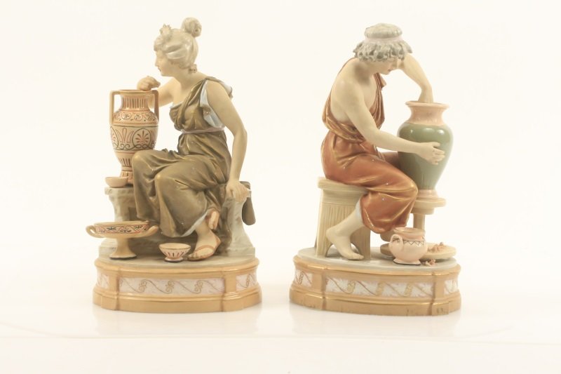 Pair of Royal Dux Figurines, Classical Potters: Royal Dux (Czech, 1860- ). A pair of porcelain figurines, circa late 19th/ early 20th century, depicting male and female classical potters, each sitting on a bench with assorted pottery on floor aroun