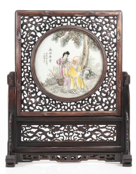 Chinese Hand Painted Table Screen, Shou/ Lan Caihe: Chinese, 20th century. A stained wood table screen with central round famille rose porcelain plaque with hand painted decoration depicting Shou, the Chinese god of longevity, at center with bulbous fo