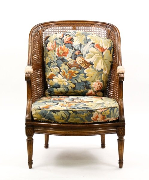 French Louis XVI Style Caned Bergere: French, late 19th/early 20th century. Louis XVI style walnut bergere having a cane upholstered back, arms and seat, raised on fluted tapering legs headed with patera blocks. The elbow rests back pillo