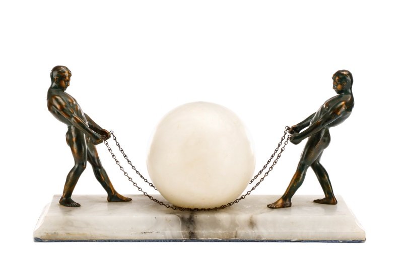 Art Deco Figural Table Lamp w/ Globe Light: Probably Continental, circa 1930s. An Art Deco figural table lamp modeled as two bronze colored semi clad men, each holding joined chains and pulling the centered circular white globe in the manner of