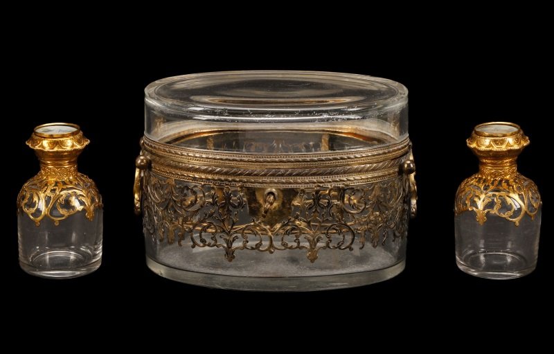 Gilt Bronze & Glass Parfumerie w/Eglomise Stoppers: French, 19th century. Likely Parisian, a gilt bronze mounted colorless glass parfumerie or fitted scent casket, the case of oval form mounted to exterior with openwork elaborate scrolling band and han