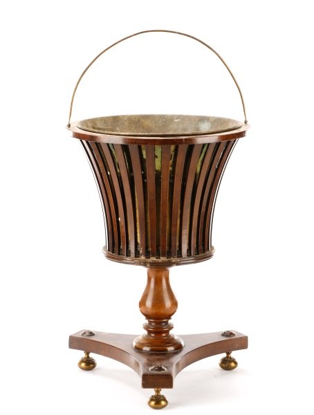 William IV Slatted Mahogany and Brass Wine Cooler: English, early 19th century. A William IV mahogany wine cooler, with a slatted tapered urn top with a conforming hammered brass insert and folding semicircular handle, atop a turned pedestal and a con