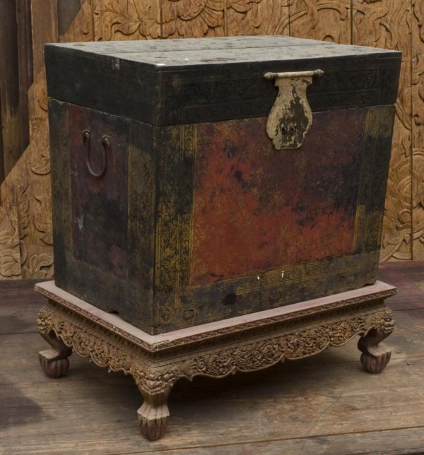 Antique Thai gilt lacquer scripture chest: Antique Thai gilt lacquer scripture chest, 18th/19th Century, of tapering rectangular form and lacquered in black and red with iron handles, 24.5"h x 30"l x 19.25"d, on red lacquered wood stand, 10"h 