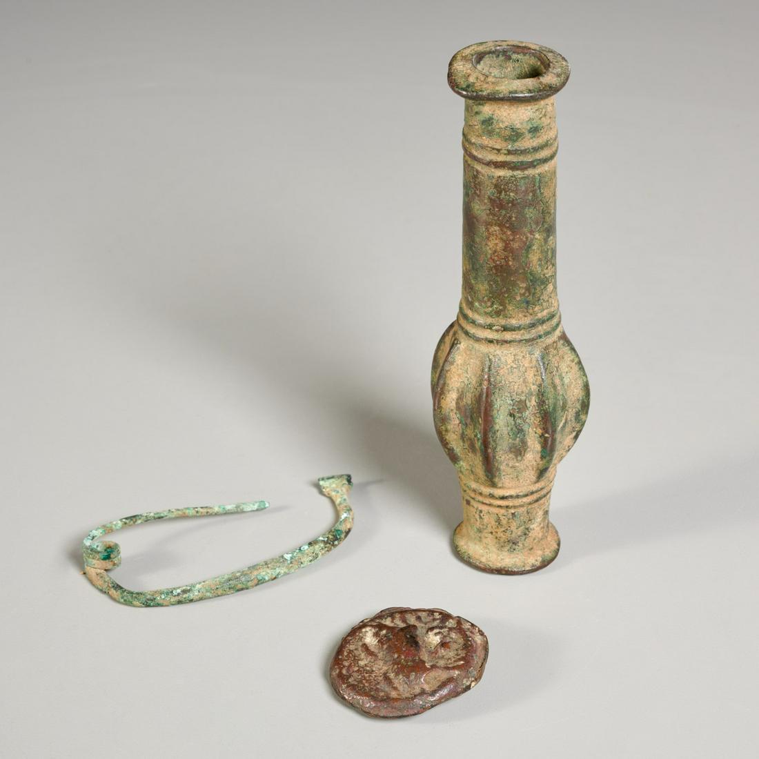 (3) bronze antiquities: (3) bronze antiquities, incl. a Near Eastern bronze mace head, prob. Luristan, a Roman bronze coiled fibula toga clasp, and an ancient bronze coin, 6"l x 2"w (largest), 1.75"dia (smallest) Provenance: