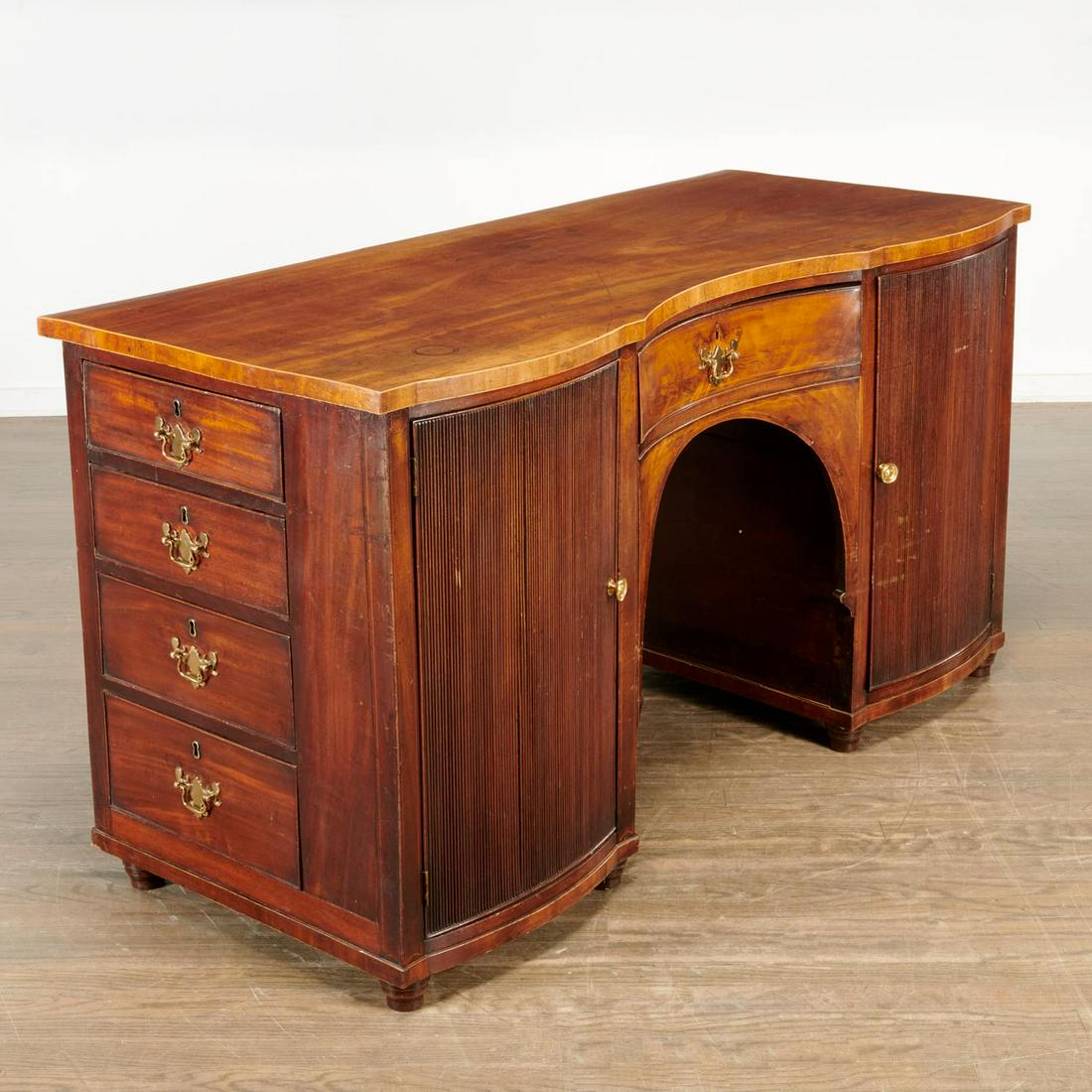 Unusual Regency mahogany tambour door desk: Unusual Regency mahogany tambour door desk, 19th c., England, with brass pulls, the shaped top over a single frieze drawer above kneehole, flanked by cabinet doors, false drawer and doors on reverse, 
