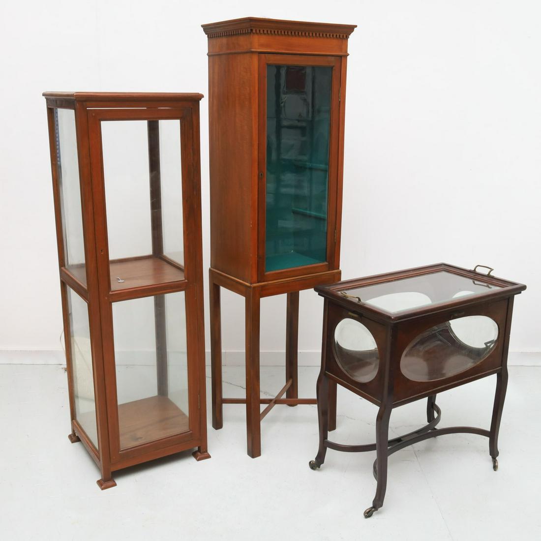 (3) antique & vintage glass front display cabinets: (3) antique & vintage glass front display cabinets, 20th c., incl. a lighted square two case display, with glass panels, a lighted display raised squared legs, and a display trolley on wheels, 17"h x