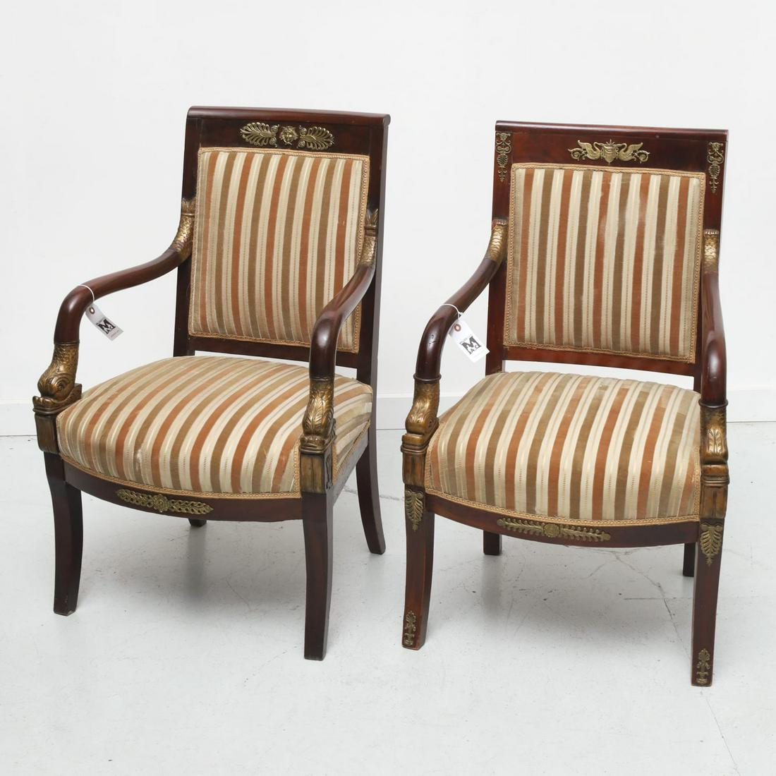 Near pair Empire style carved mahogany armchairs: Near pair Empire style carved mahogany armchairs, 20th c., heavy mahogany, with carved and gilt dolphin arms, applied gilt metal decoration to top rail, neutral sculpted upholstery to seats and backs,