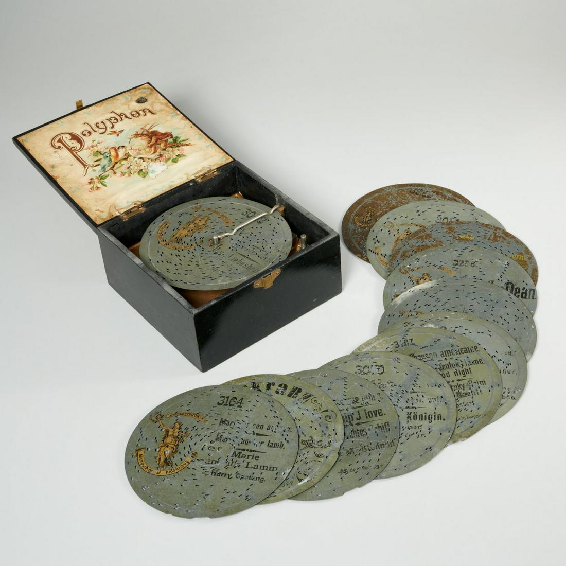 Polyphon music player and disks: Polyphon music player and disks, Late 19th/Early 20th c., Germany, black lacquered wood case, with celluloid panel to lid with cherubs in lower relief, the lid interior paper lined, with (11) extra di