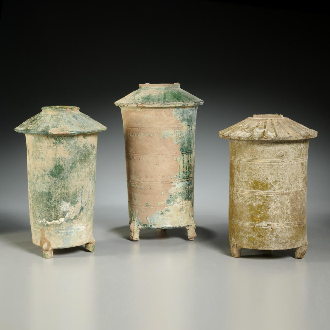 (3) early Chinese green glazed granary jars: (3) early Chinese green glazed granary jars, Likely Han Dynasty (2nd c. BCE- 3rd c. ADE), in the form of a granary silo with tiled roof, raised on tripod feet, 14.75"h x 8"dia (largest), 12.25"h x 8"d