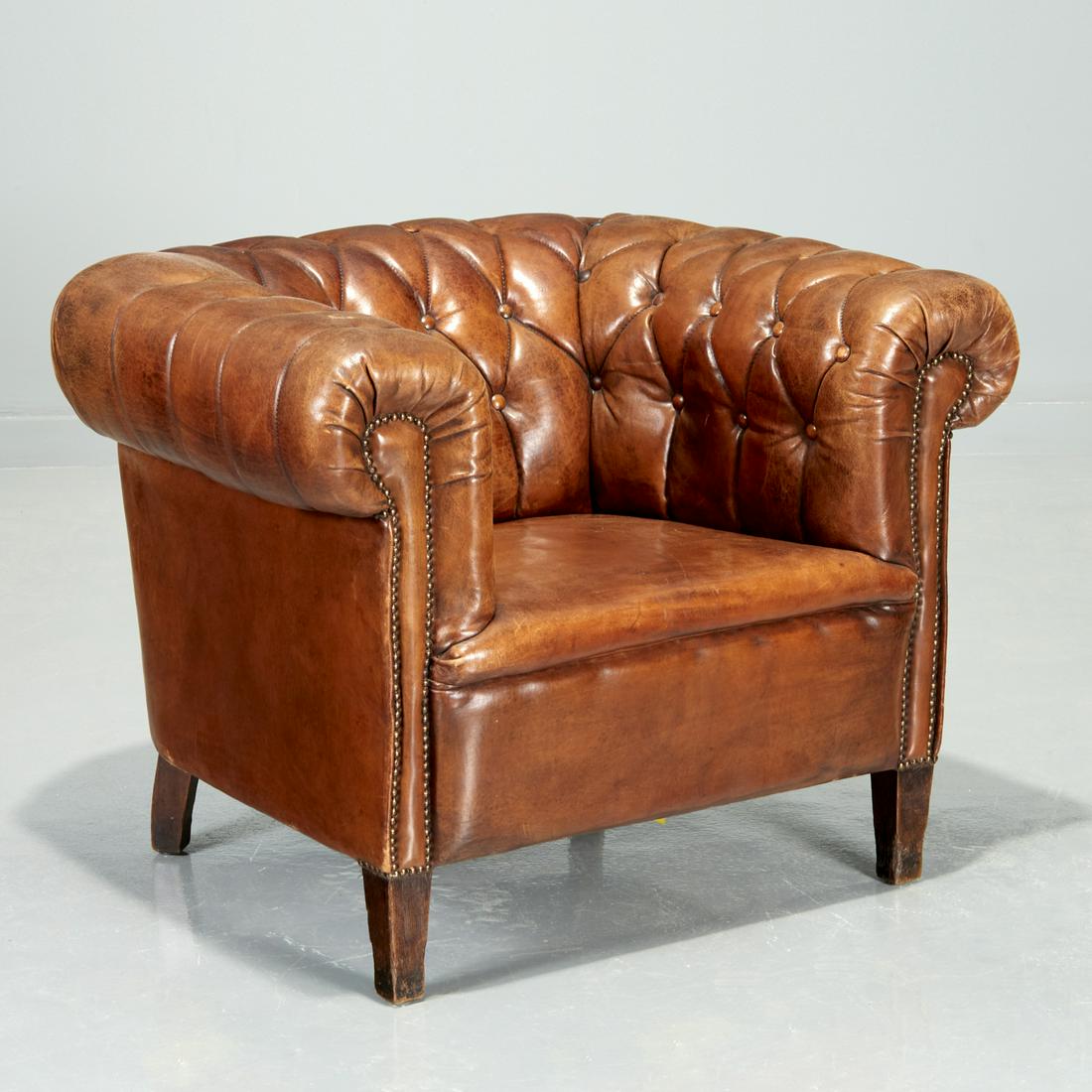 Edwardian leather Chesterfield club chair: Edwardian leather Chesterfield club chair, Early 20th c., England, button-tufted brown leather back, armrests and seat, brass rivets, raised on square tapering stained oak legs, 29"h x 36"w x 31"d, 18