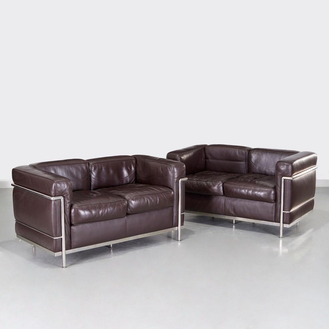 Corbusier (after), pair LC2 style 2-seat settees: Corbusier (after), pair LC2 style 2-seat settees, Introduced c. 1928/1990s, chromed tube metal frame, brown leather back, seat and side cushions, cloth label to decking, 27"h x 51"w x 28"d