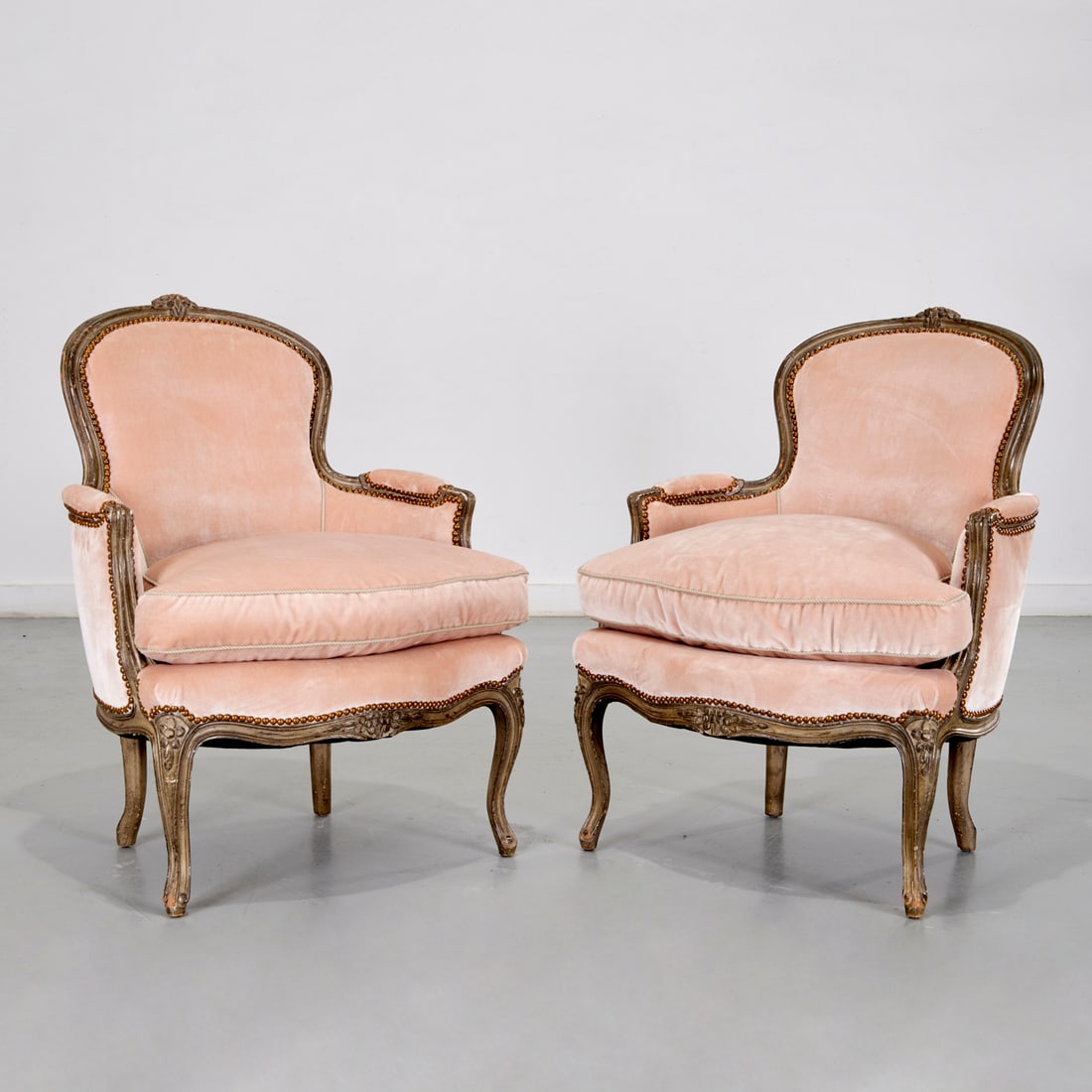 Pair Louis XV style grey painted bergeres: Pair Louis XV style grey painted bergeres, Mid 20th c., France, channel carved and painted wood frame, the padded back, seat and armrests upholstered in a pink velvet mohair, brass tack border, with d